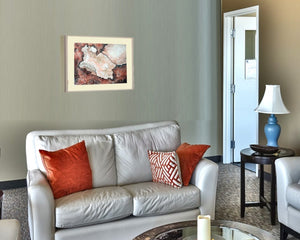 Aquarell Edition Artefakte von johann franki in einem Wartezimmer mit Couch und Tisch.Das  Motiv im Querformat zeigt ein helles Artefakt auf altrotem, zerfurchten Hintergrund, gerahmt mit Passepartout.